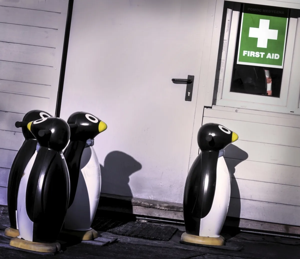 Three penguin-shaped skating aids outside a door beneath a first aid sign